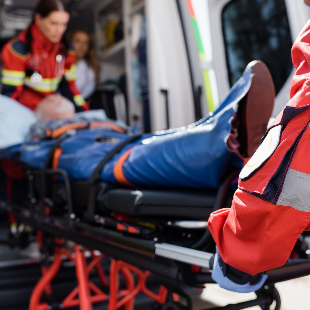 Des ambulanciers chargent un patient sur une civière dans une ambulance ; un ambulancier porte une veste rouge.