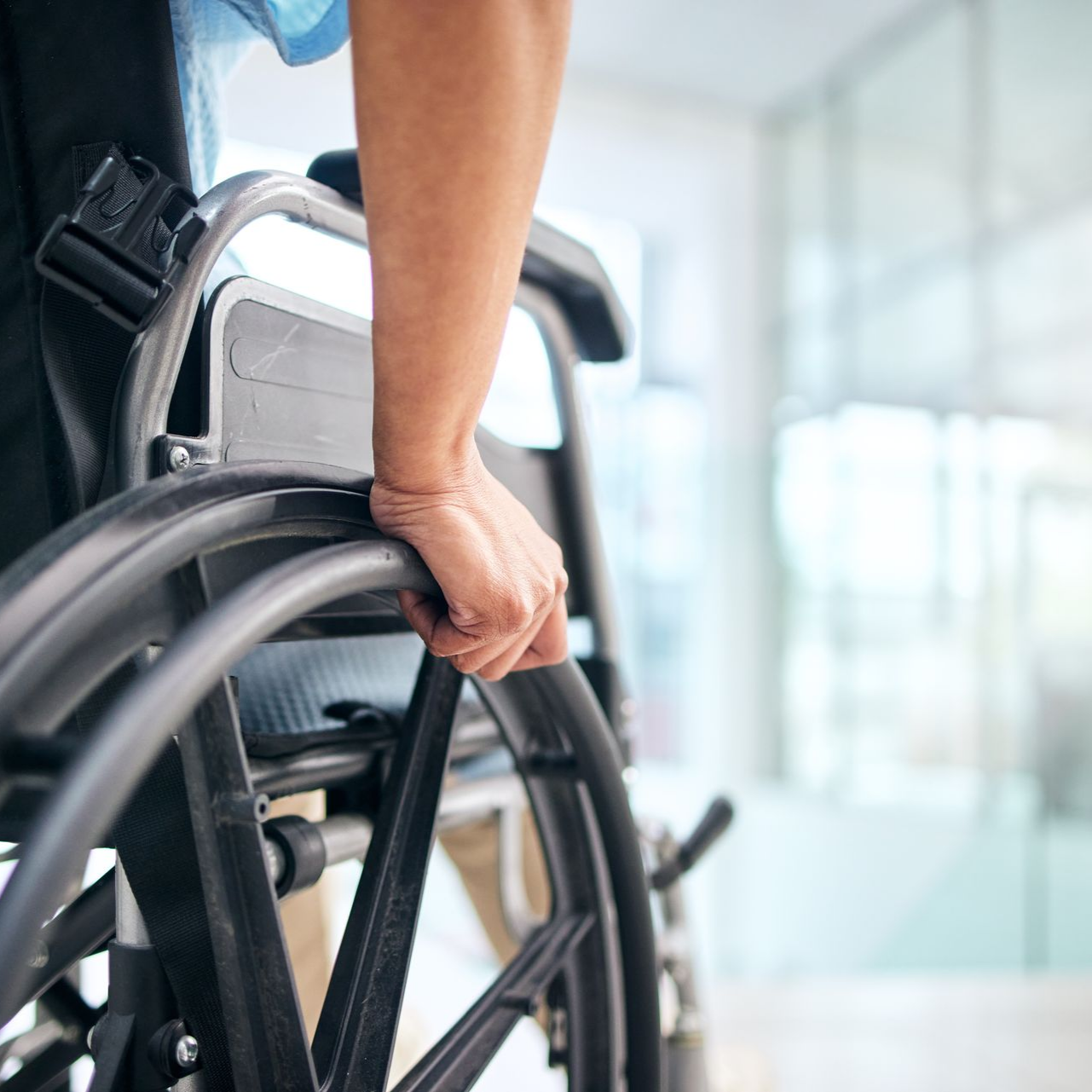 La main d'une personne sur la roue d'un fauteuil roulant à l'intérieur d'un bâtiment, probablement un établissement médical.