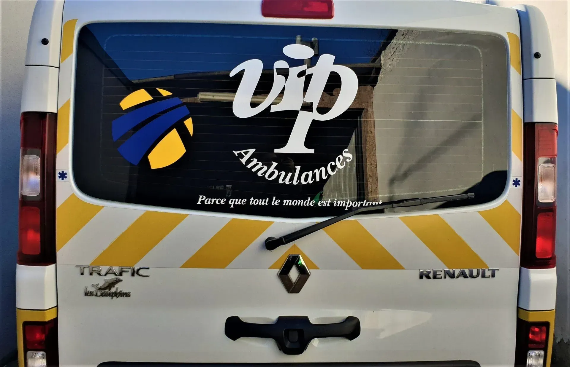 Arrière d'une fourgonnette blanche. Le design comprend un logo et du texte. Bandes en chevrons jaunes.