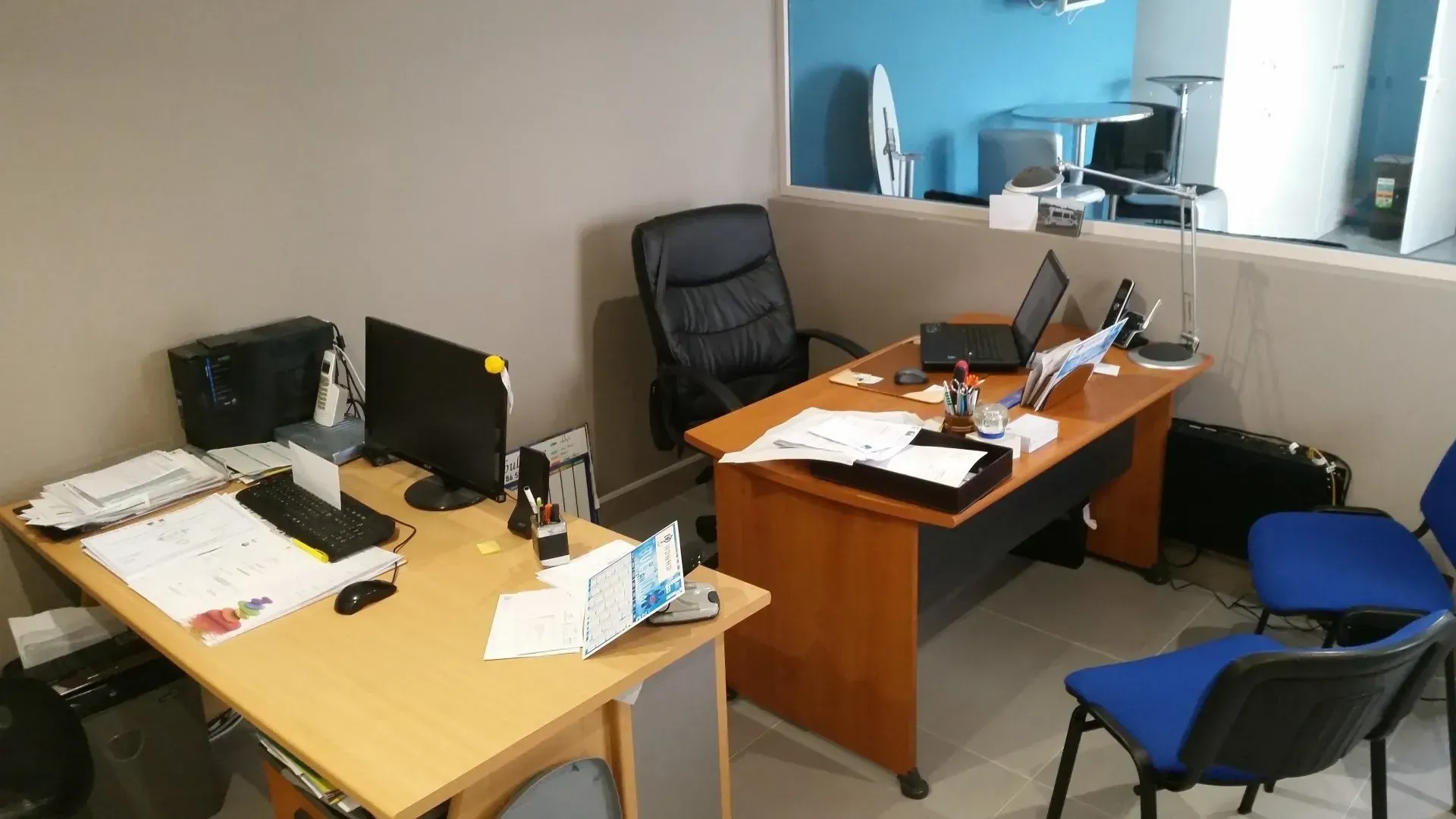 Espace de bureau avec bureaux, ordinateurs et chaises ; un poste de travail avec un écran et un bureau avec des documents.