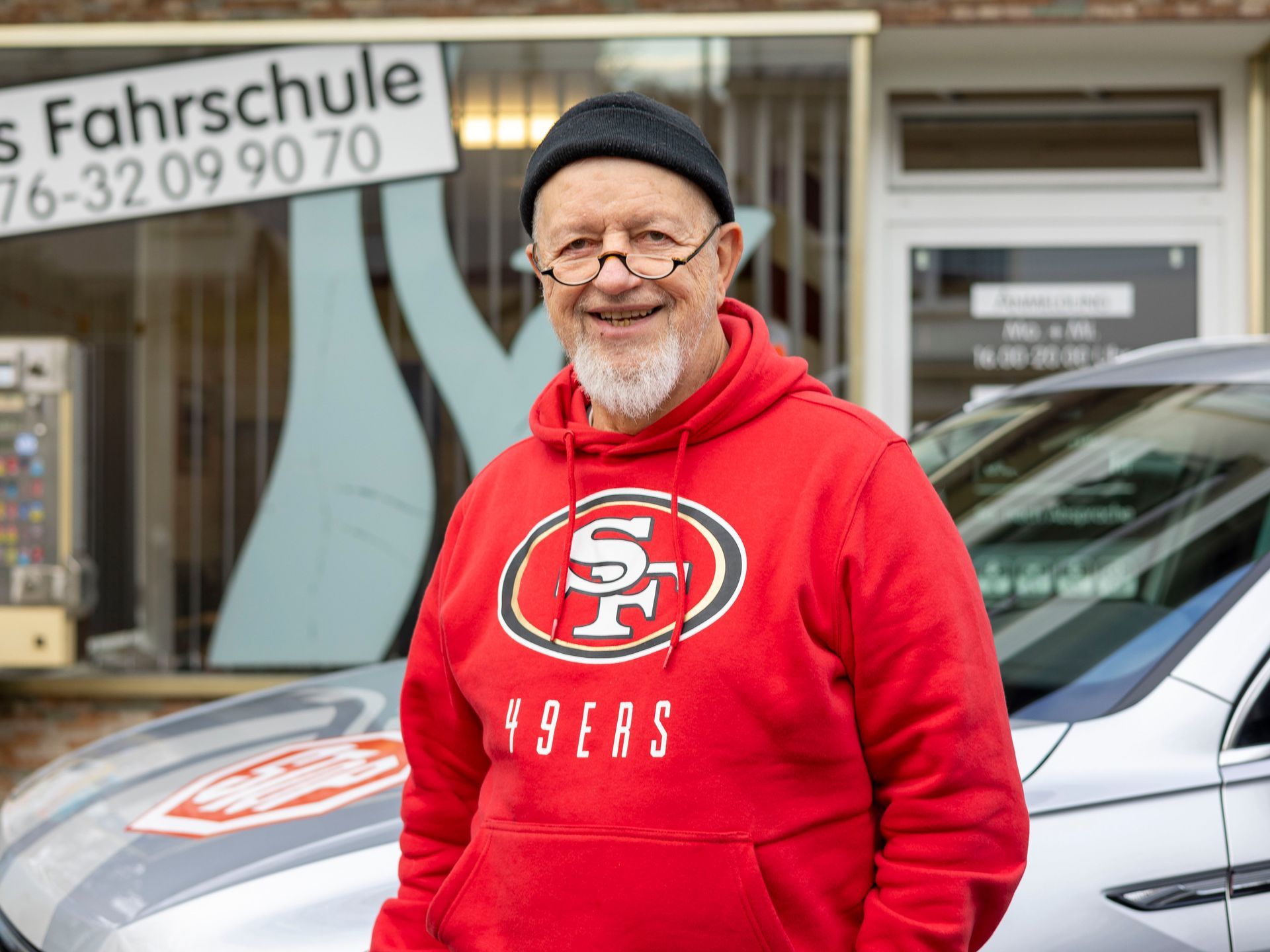 Ein Mann mit einem roten 49ers-Kapuzenpullover steht vor einem Auto.
