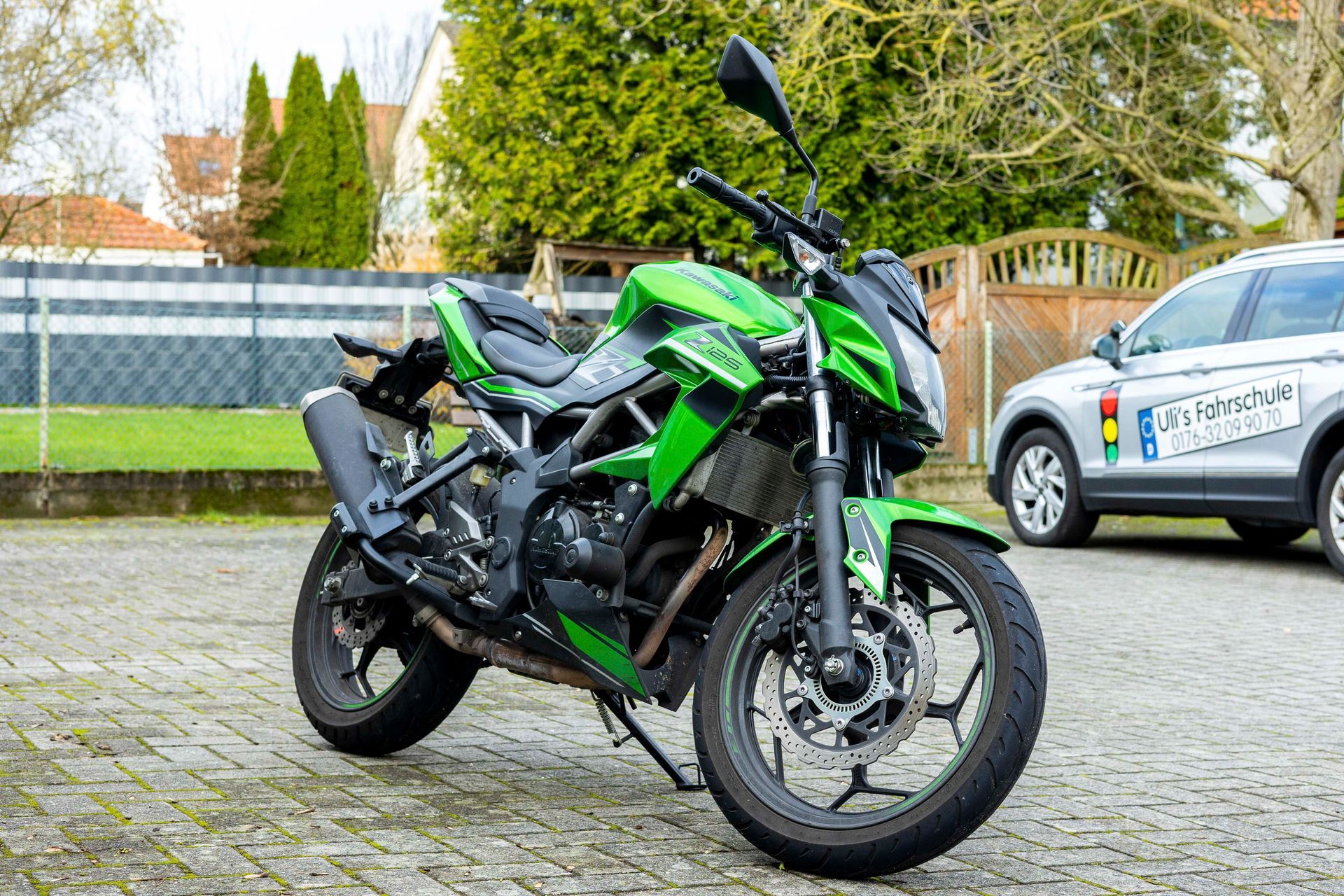 Ein grünes Motorrad parkt neben einem silbernen Auto.