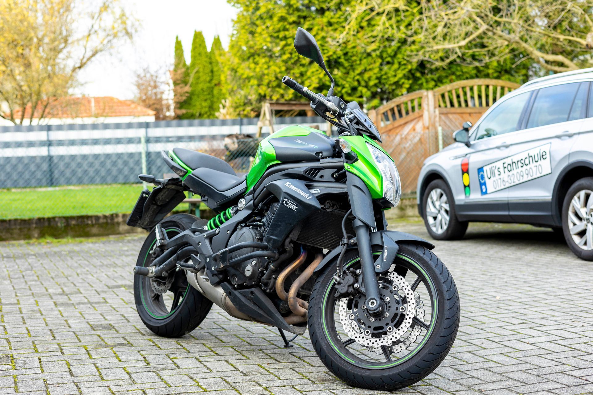 Ein grün-schwarzes Motorrad parkt neben einem silbernen Geländewagen.