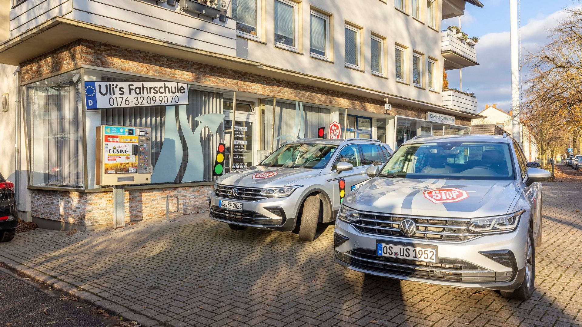 Zwei Autos sind vor einem Gebäude in einer Kopfsteinpflasterstraße geparkt.