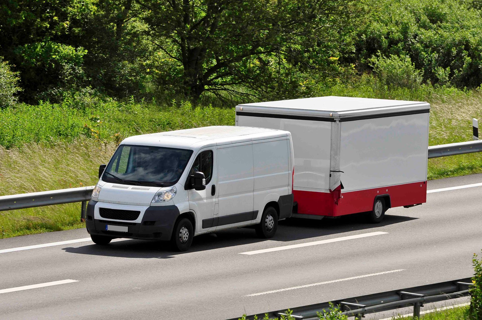 Ein weißer Lieferwagen zieht einen Anhänger auf einer Autobahn.