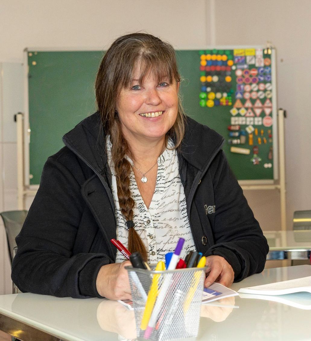 Eine Frau sitzt lächelnd an einem Schreibtisch mit einem Stifthalter