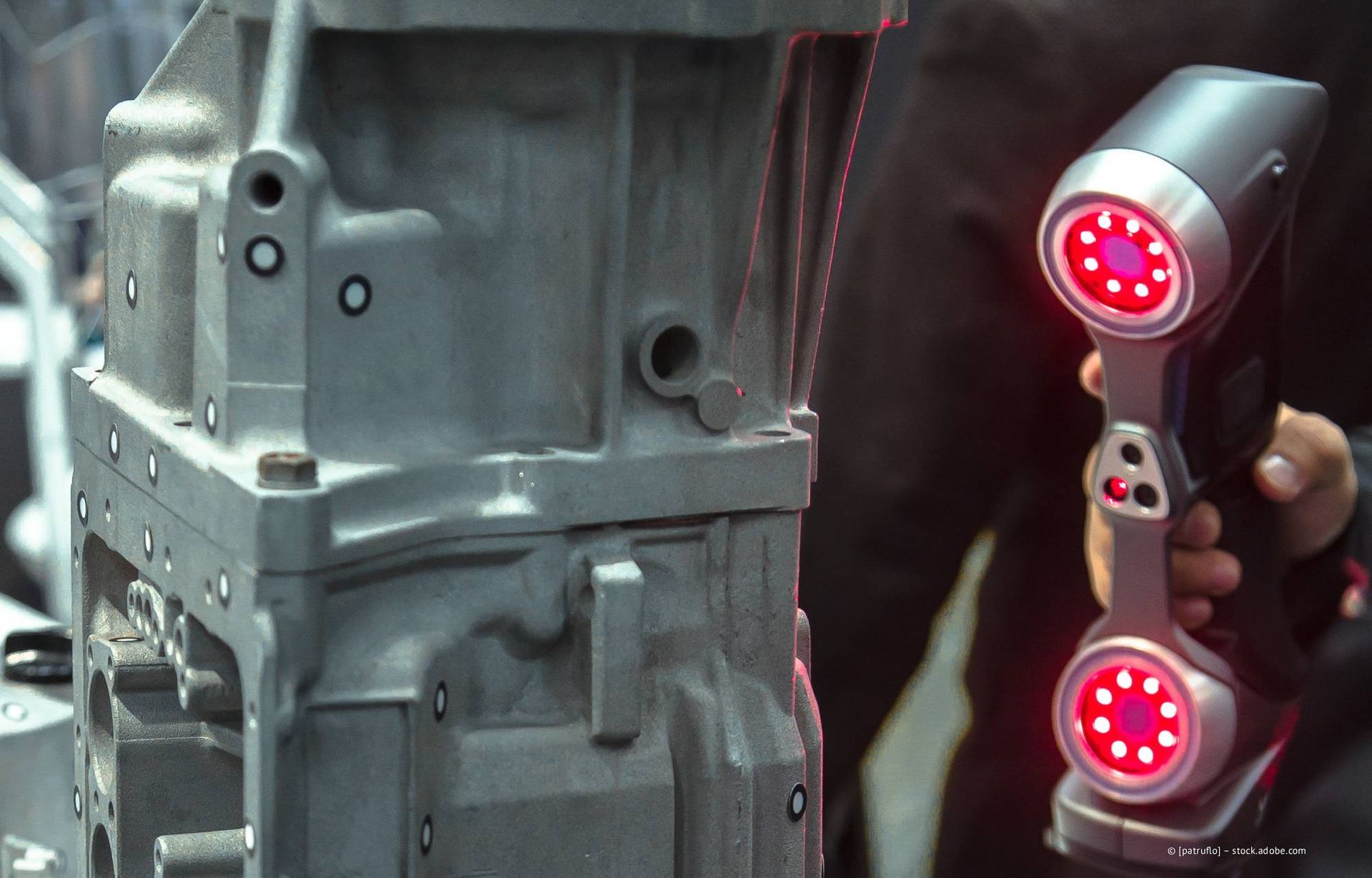 Eine Person benutzt einen handgeführten 3D-Scanner an einem grauen Industrieteil mit weißen Markierungen.