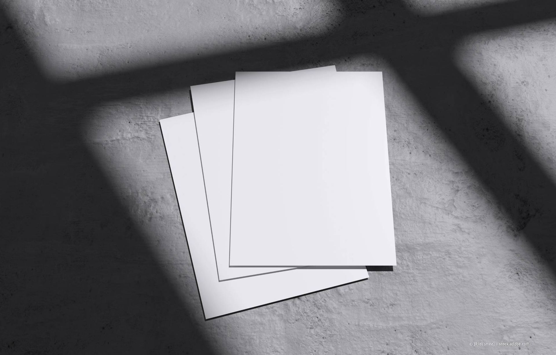 Drei weiße Blätter Papier auf einer Betonfläche, die einen Schatten werfen.