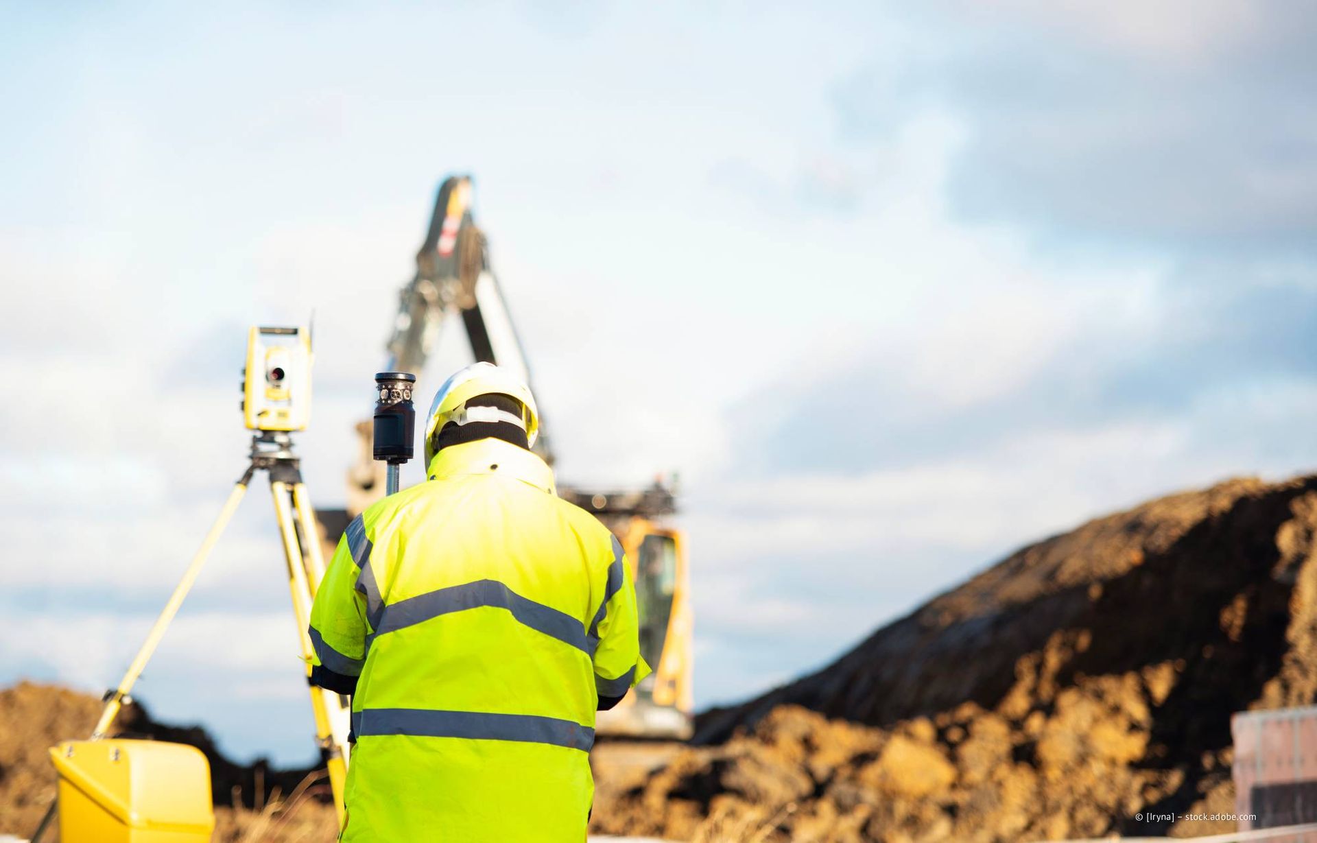 Ein Vermesser in gelber Sicherheitsweste bedient Vermessungsgeräte auf der Baustelle.