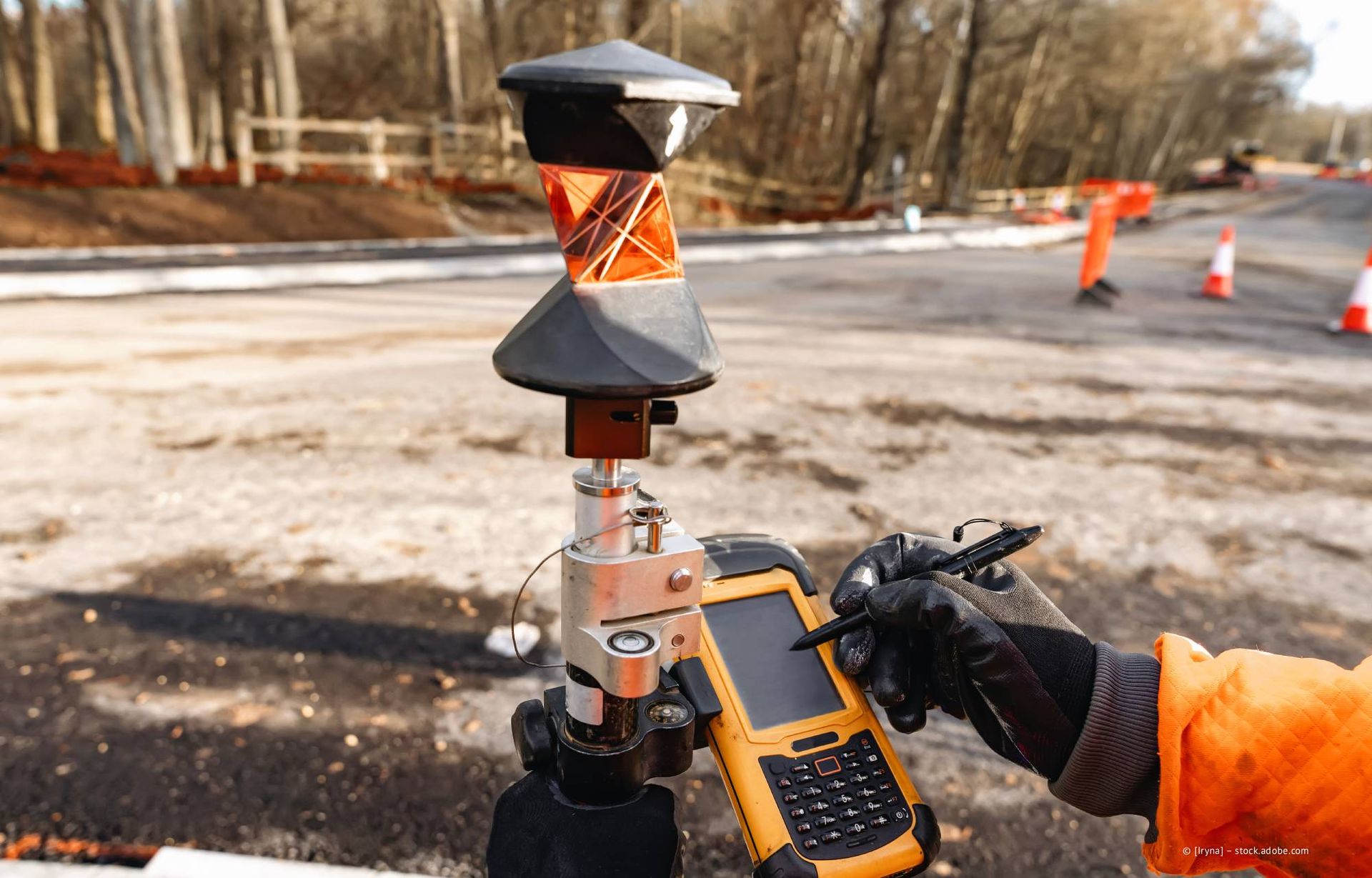 Vermesser, der auf einer Straßenbaustelle ein Handgerät mit Vermessungsprisma verwendet.