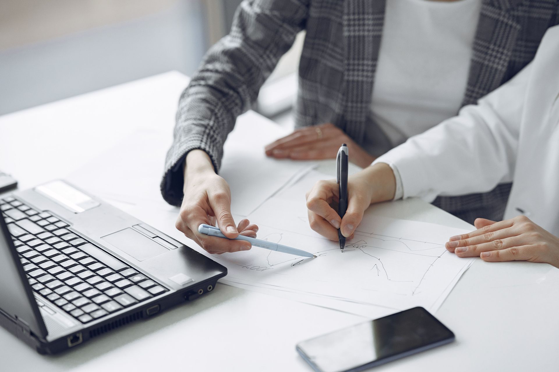 Manos revisando un plano sobre un escritorio, con un portátil y un teléfono inteligente cerca