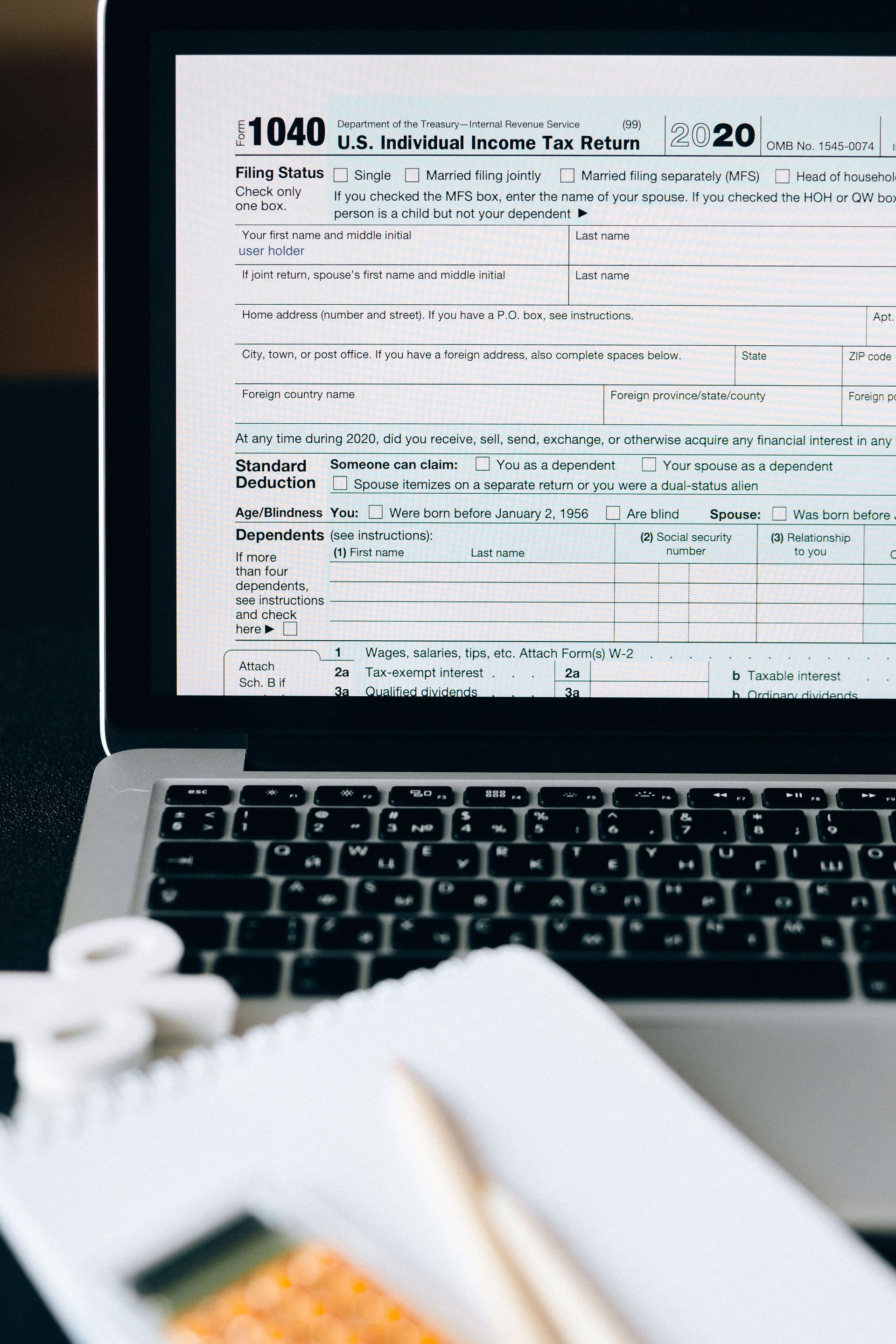Un portátil con un formulario fiscal en la pantalla, junto a un bloc de notas y un lápiz sobre un escritorio