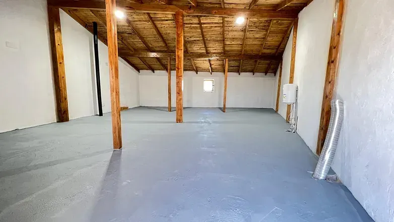 Un ático vacío con vigas de madera y suelo gris.