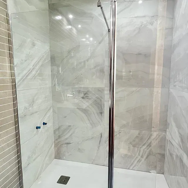 Un baño con azulejos de mármol y una ducha a ras de suelo con puerta de cristal.