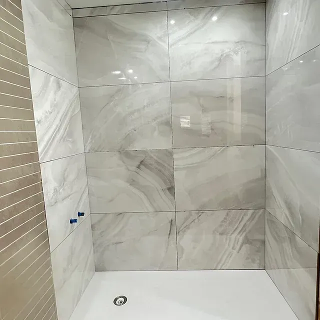 Un baño con azulejos de mármol y ducha a ras de suelo.