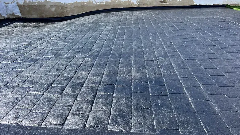 Un camino de entrada de ladrillo negro con una pared blanca al fondo.
