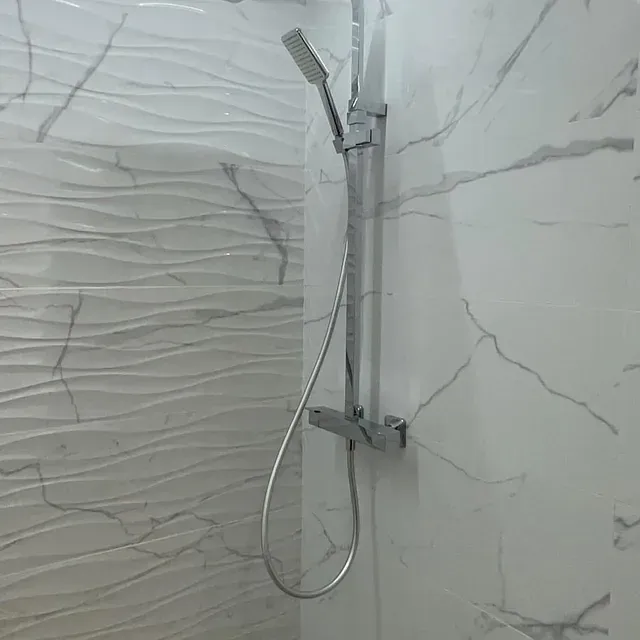 Hay un cabezal de ducha en la ducha con azulejos de mármol en la pared.
