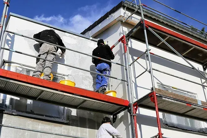 Dos hombres están pintando el costado de un edificio sobre un andamio.