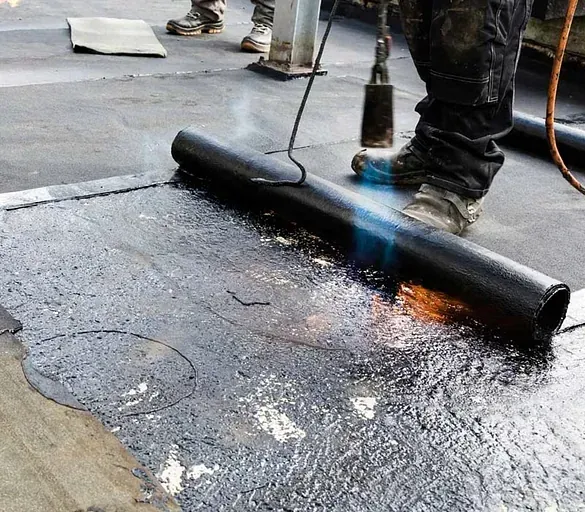 Una persona está usando una antorcha para extender un trozo de asfalto sobre un techo.