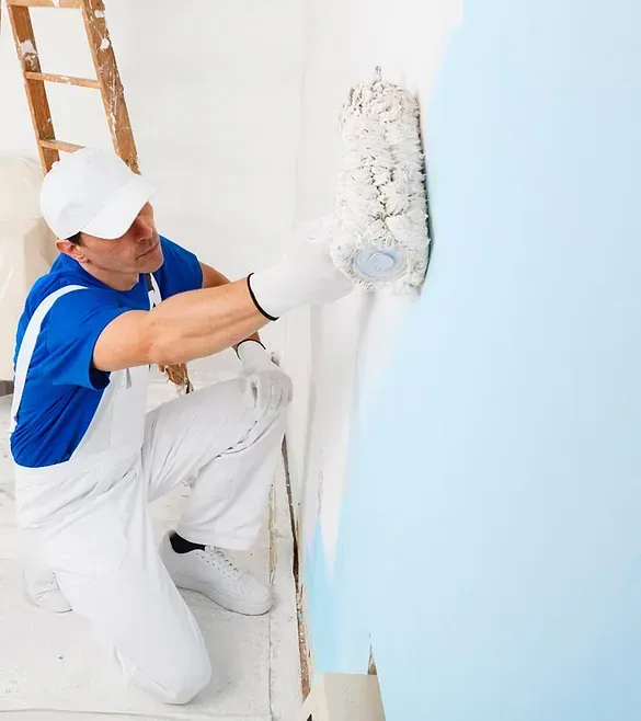 Un hombre está arrodillado y pintando una pared de azul.