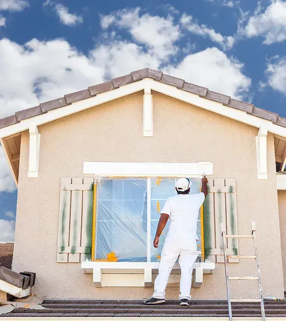 Un hombre está pintando una ventana en el costado de una casa.