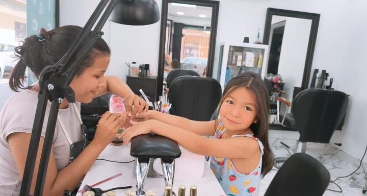 A una niña le están pintando las uñas una mujer en un salón.