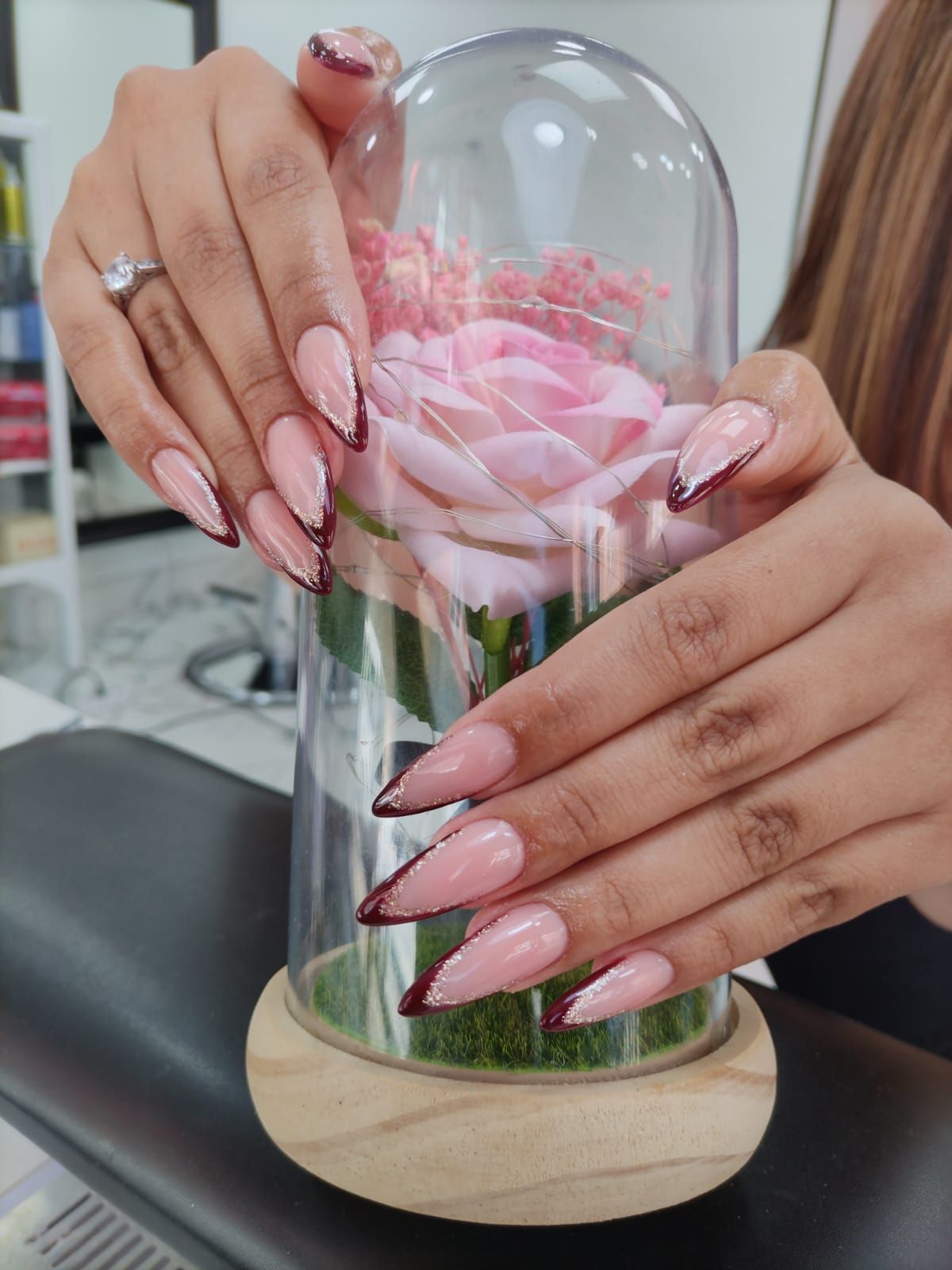 Una mujer con uñas largas sostiene una rosa rosada en una cúpula de cristal.