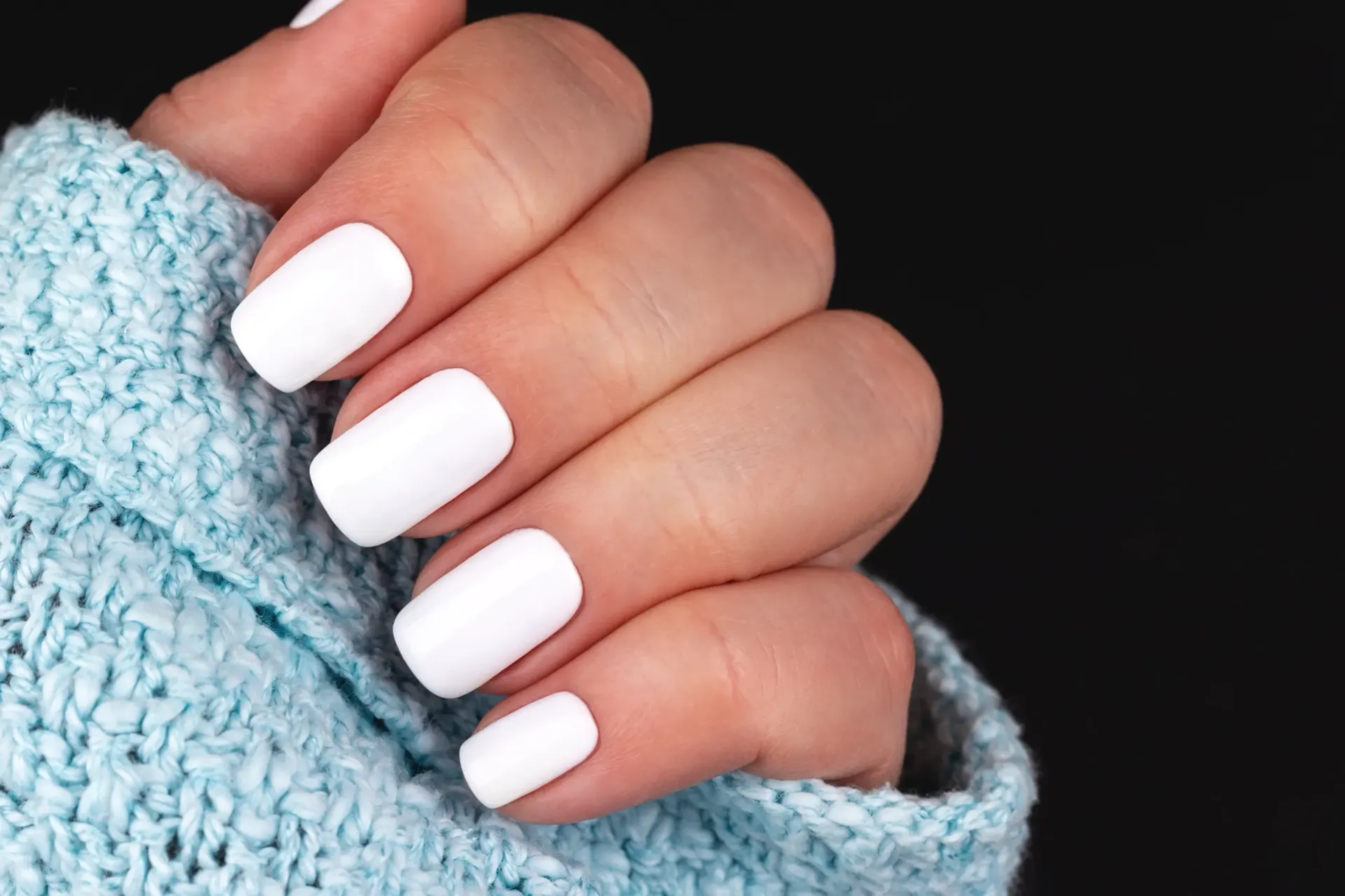 Un primer plano de la mano de una mujer con uñas blancas y un suéter azul.