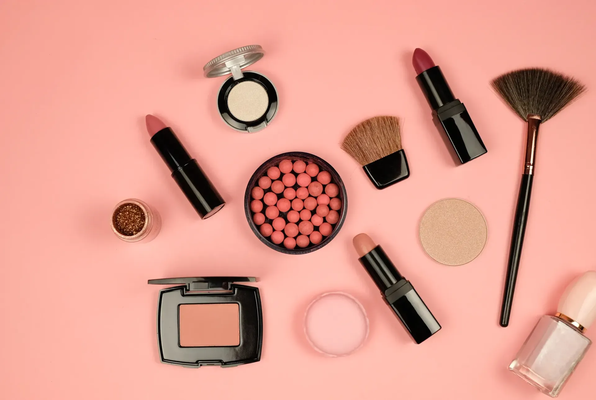 Una variedad de productos de maquillaje están dispuestos en un círculo sobre un fondo rosa.