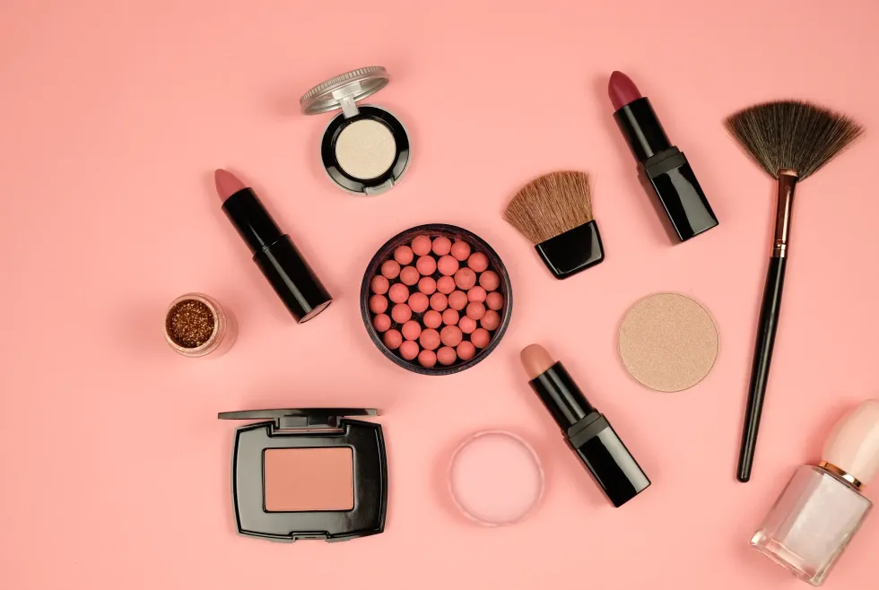 Una variedad de productos de maquillaje están dispuestos en un círculo sobre un fondo rosa.