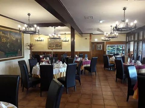 Elegante comedor de restaurante con mesas redondas, manteles blancos, sillas oscuras e iluminación cálida en las paredes.
