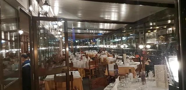 Comedor de restaurante con paredes de cristal, manteles blancos y mesas preparadas para el servicio nocturno.