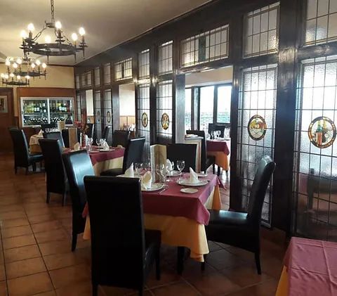 Tranquilo comedor de restaurante con mesas puestas, sillas negras y grandes ventanales a lo largo de la pared.
