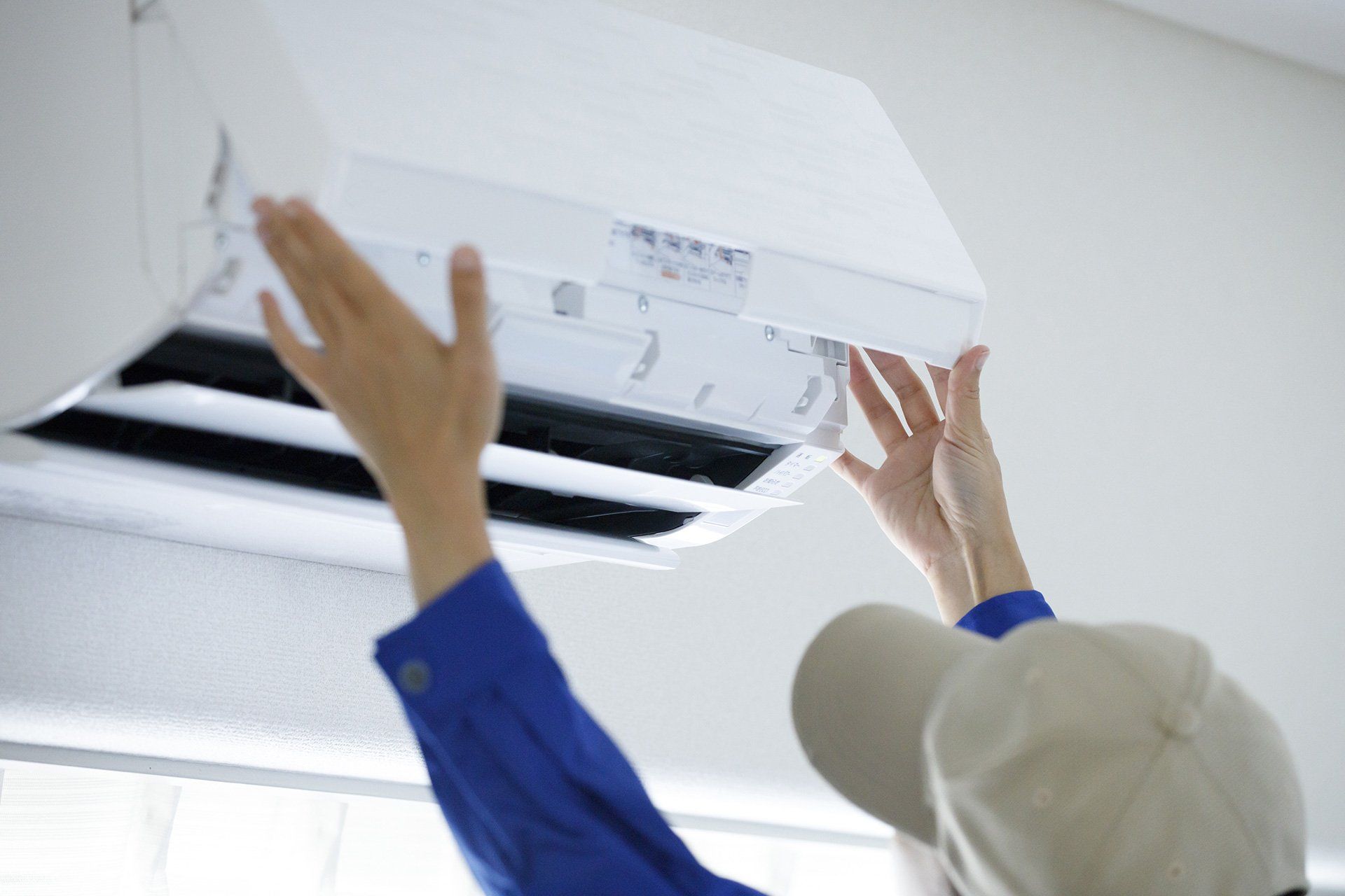 Persona instalando un aire acondicionado de techo blanco con los brazos en alto en una habitación luminosa.