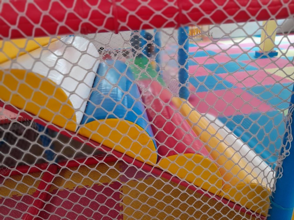 Estructura de juego inflable de colores detrás de una red de seguridad roja en un área de juegos interior.