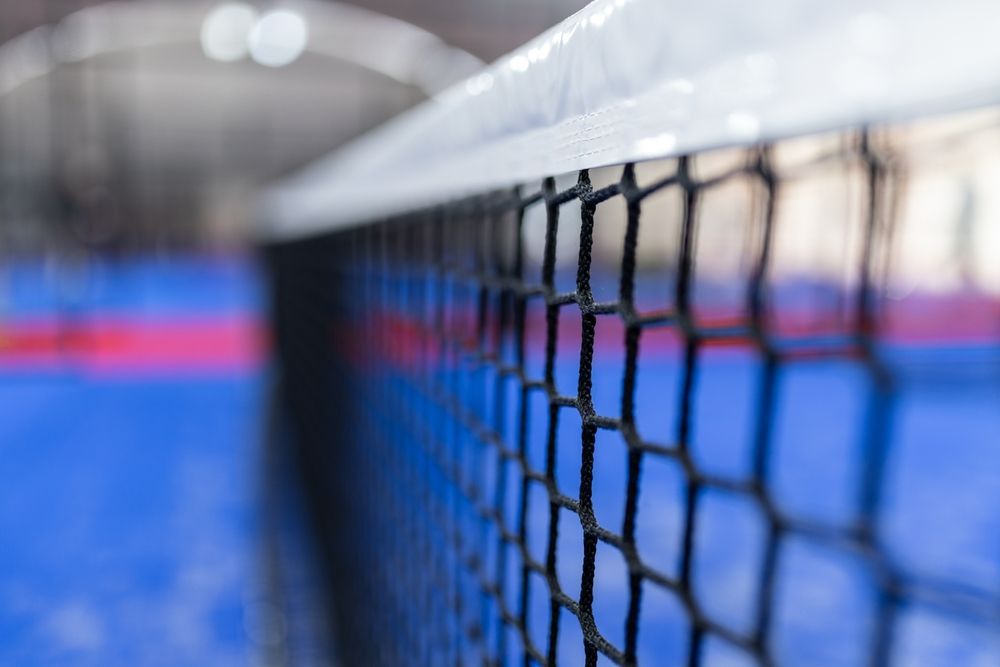Primer plano de una red de tenis en una cancha azul con un fondo interior desenfocado.