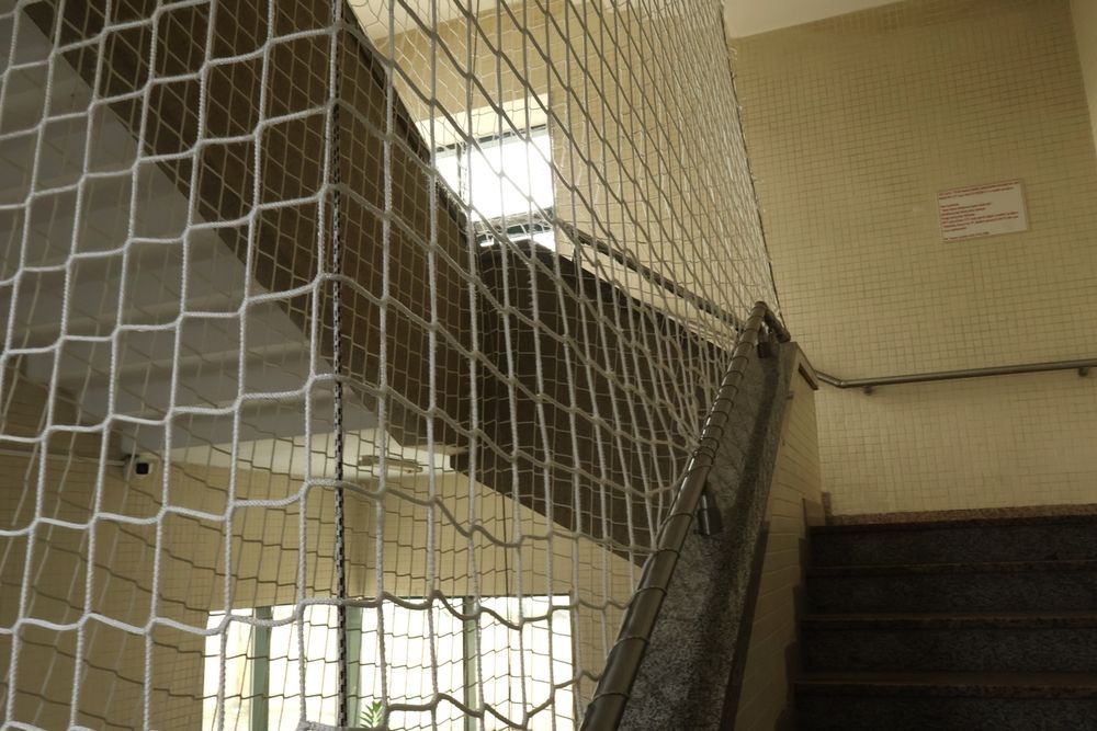 Malla metálica dañada a lo largo de una escalera interior, con una sección rota y escombros en el suelo.