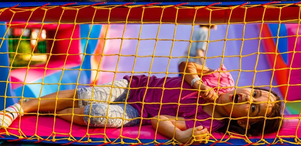 Niño tumbado sobre un hinchable rosa dentro de una colorida zona de juegos con red.