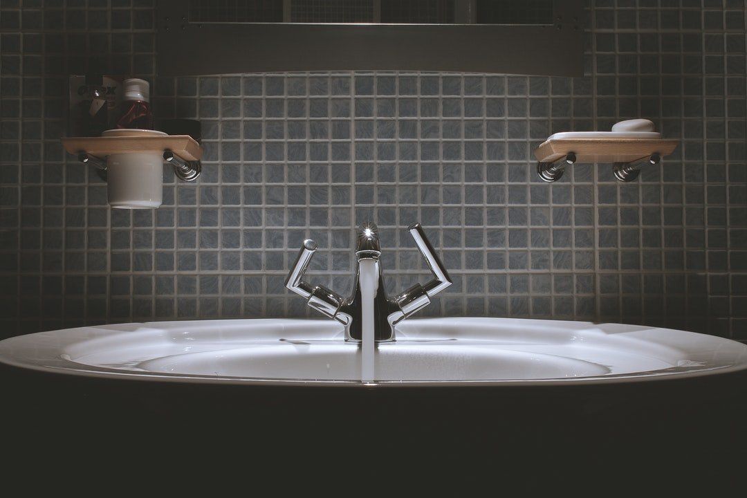 Lavabo moderno con grifo cromado y dos apliques de pared sobre un salpicadero de azulejos.