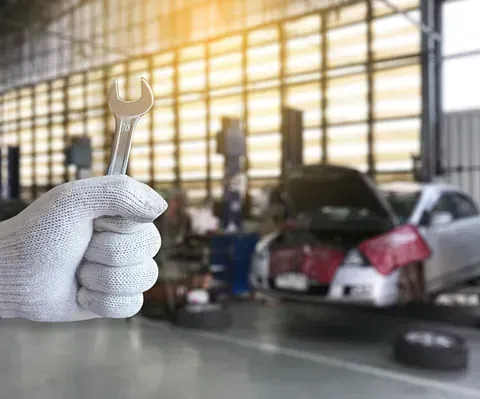 Una mano sostiene una llave inglesa delante de un coche en un garaje.