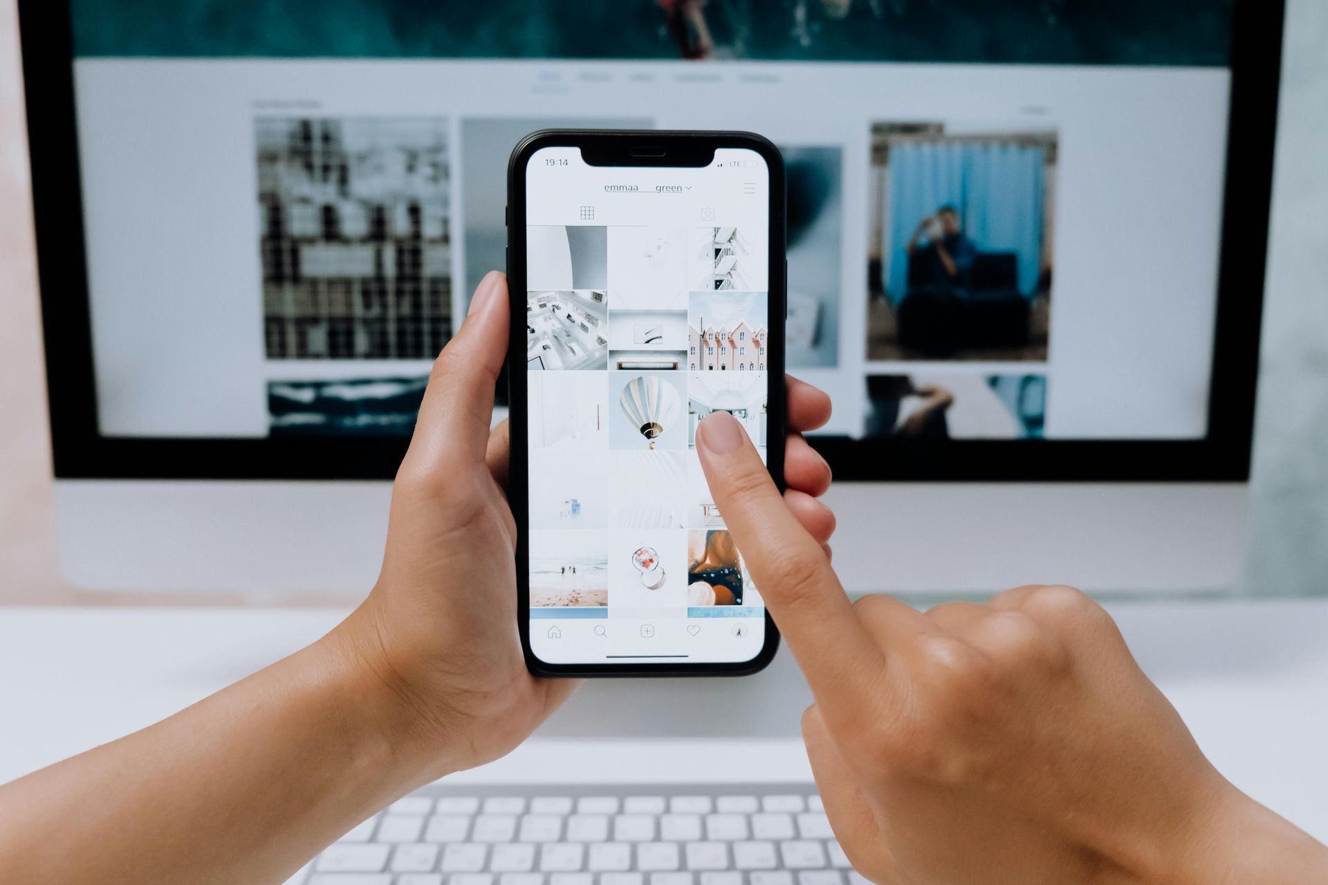 Una persona tiene in mano un telefono cellulare davanti a un computer.