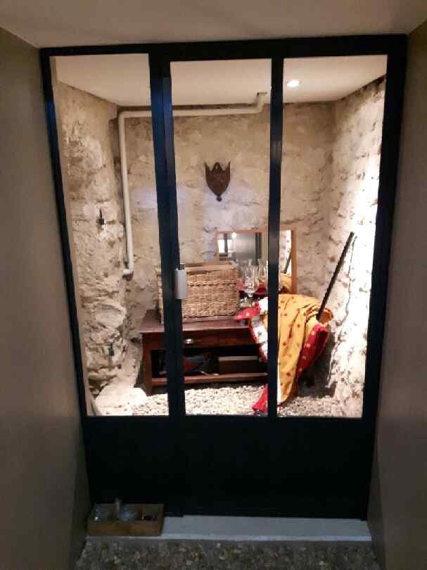 Pièce endommagée avec des débris, des murs apparents, une chaise et une petite table visibles à travers une porte sombre.