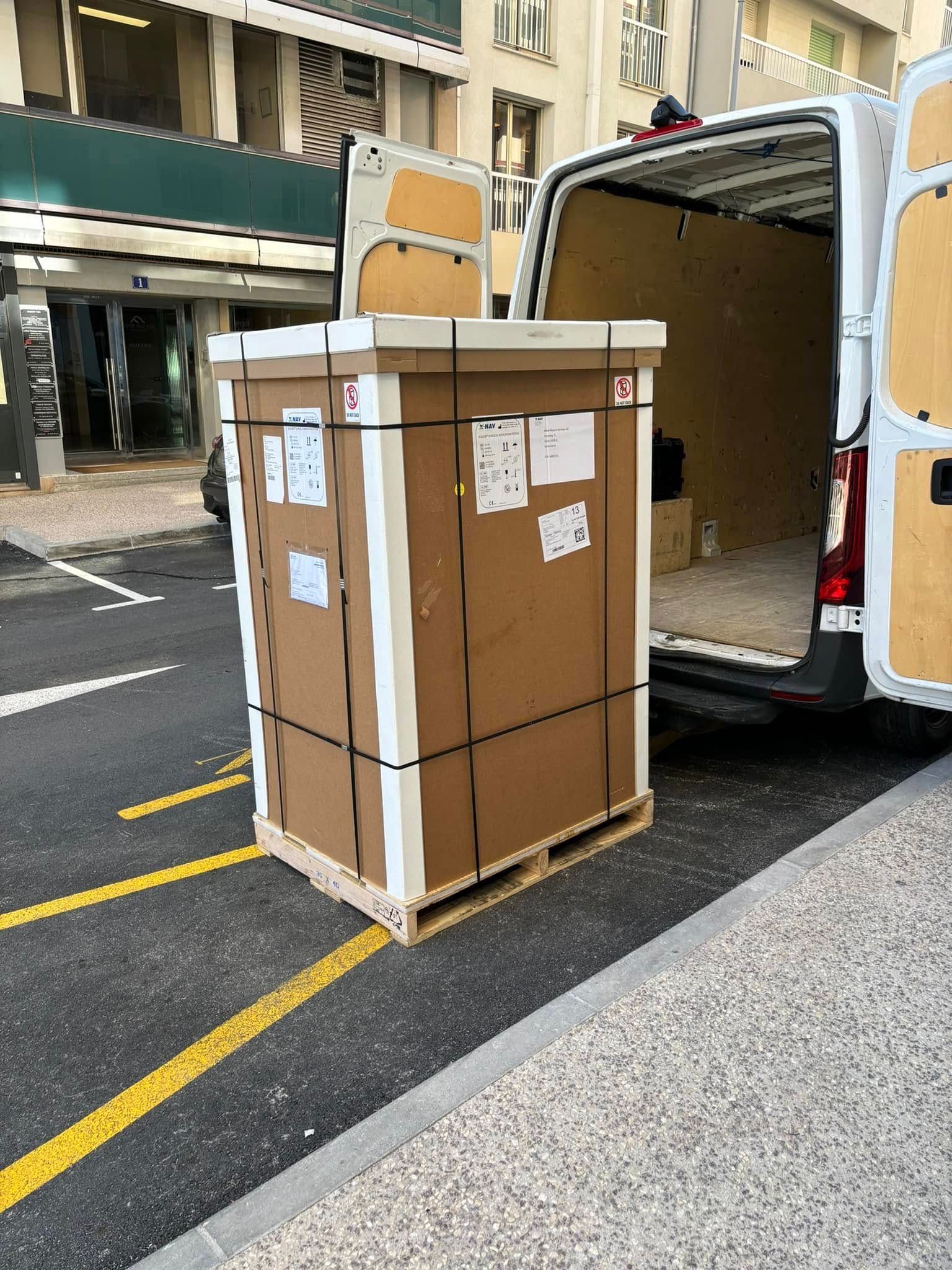 Caisse de transport devant un camion de déménagement blanc avec les portes arrière ouvertes.