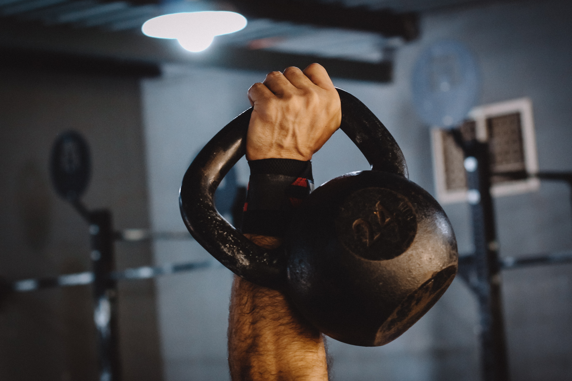 Un homme tient une kettlebell au-dessus de sa tête dans une salle de sport.