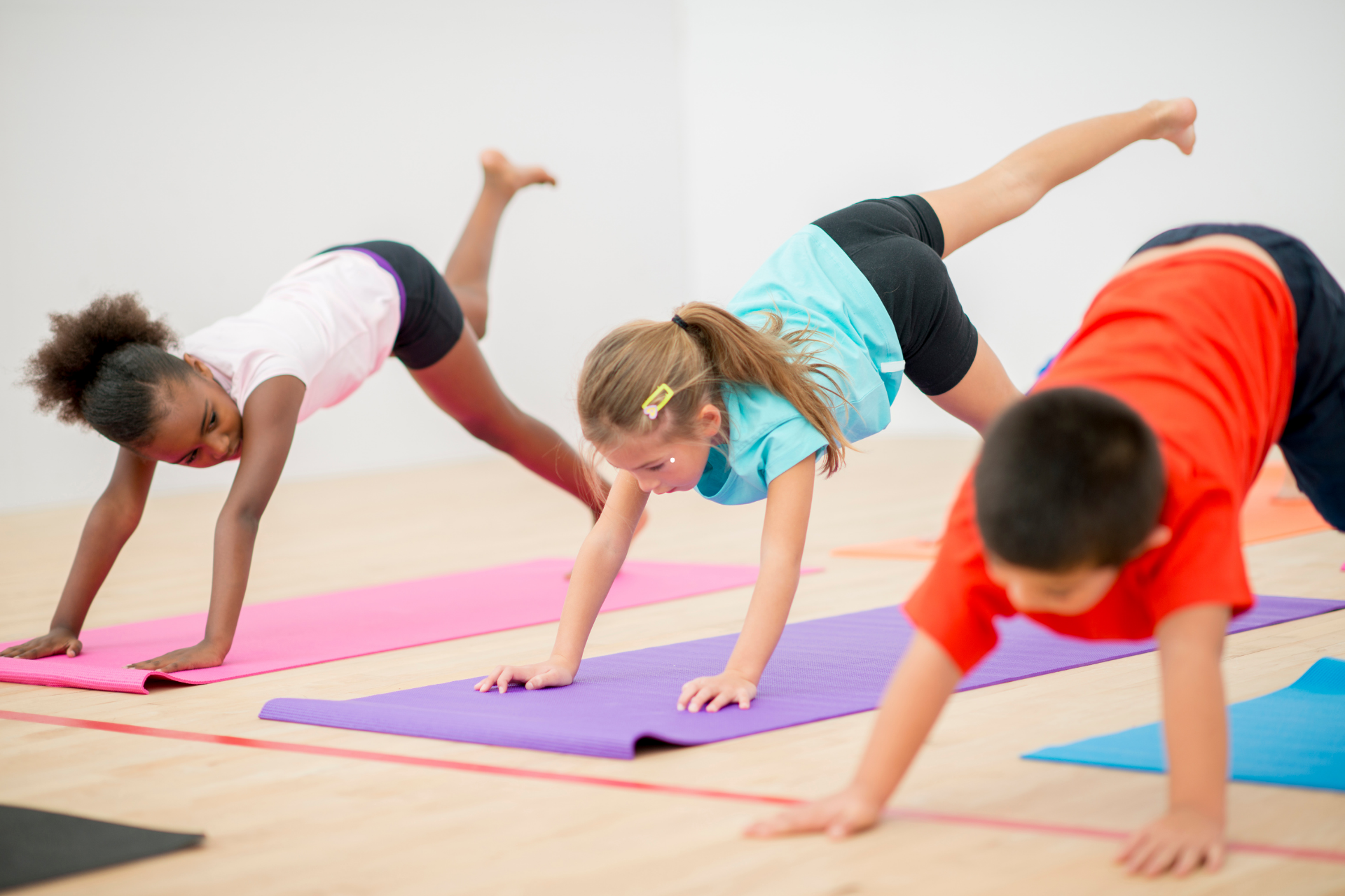 Un groupe d'enfants font du yoga sur des tapis dans une salle de sport.