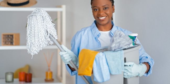 Woman holding cleaning supplies and smiling.