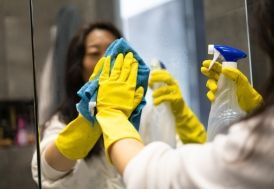 Woman spraying and wiping a window, wearing gloves and smiling.