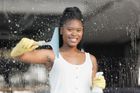 Woman cleaning a window with a squeegee and spray bottle, smiling.