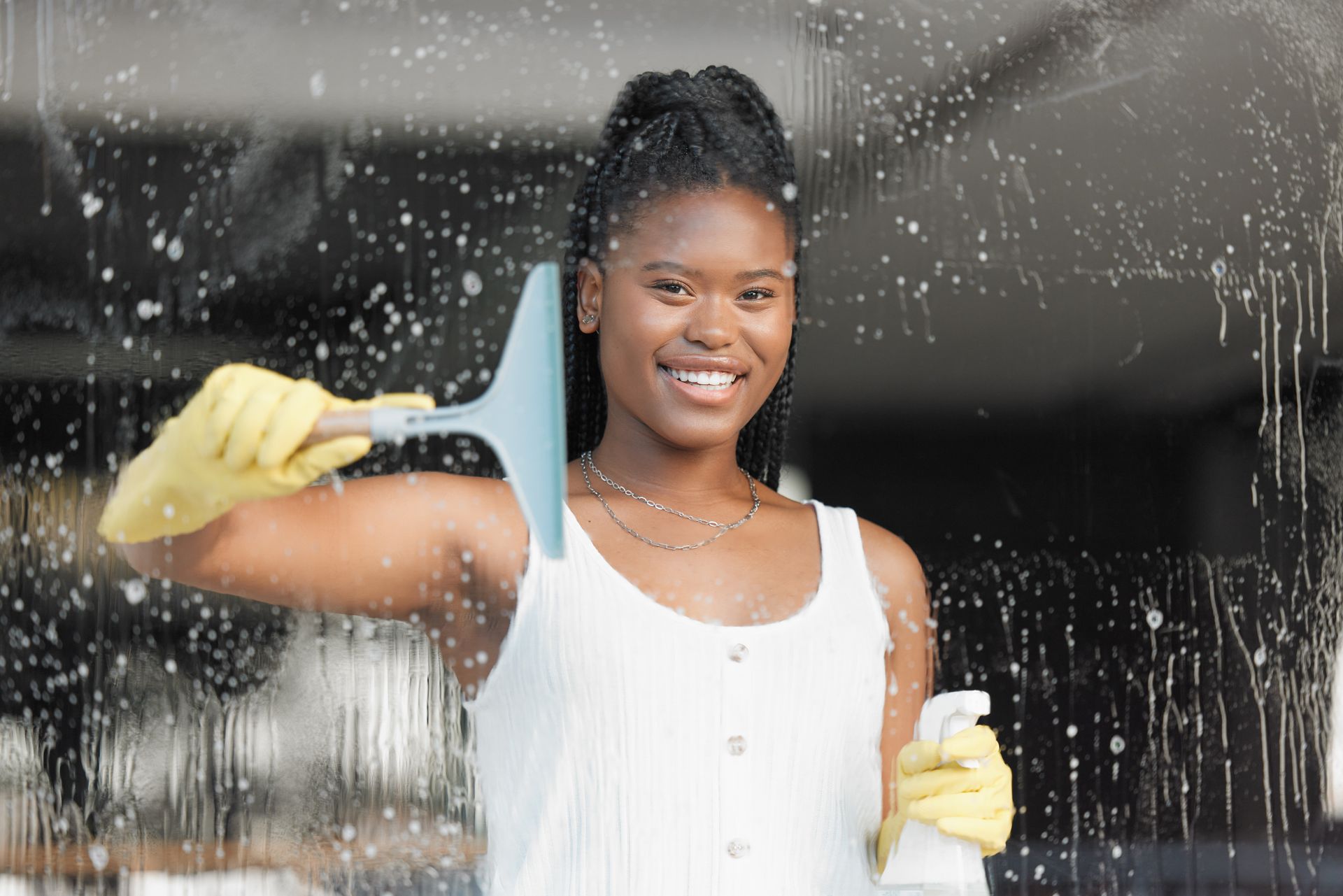 Woman cleaning a window with a squeegee and spray bottle, smiling.