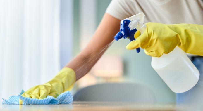 Woman holding a mop and cleaning supplies, smiling, indoors.